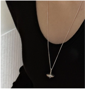 Macro shot of minimalist silver spinning top pendant on a long chain worn by model