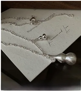 Macro detail of silver gourd pendant with matte brushed finish and tiny diamond accent