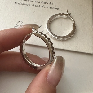 S925 sterling silver hoop earrings with a scalloped edge design held by hand