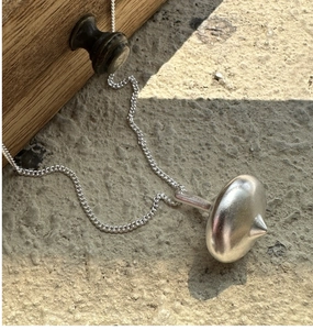 Close-up of a silver spinning top pendant on a fine chain over a textured stone surface