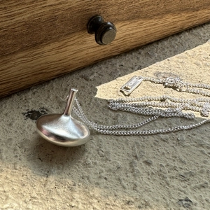 Minimalist S925 sterling silver spinning top pendant necklace on a grey stone background