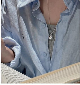 Detail of silver bead necklace with spherical pendant worn on a collarbone