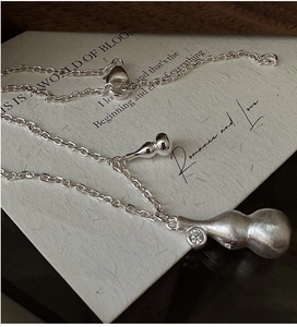 Macro detail of brushed silver gourd pendant with zircon on a vintage paper background