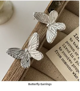 Macro shot of silver butterfly earrings with detailed wing texture on a wooden box