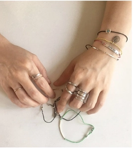 Close-up of stacked S925 sterling silver twist rings and colorful woven cord bracelets