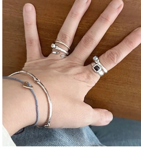 Dettaglio di anelli in metallo misto e braccialetto blu con cuore sulla mano