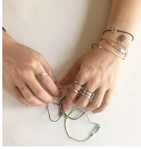 Close-up of stacked S925 sterling silver twist rings and colored cord charm bracelets