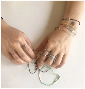 Macro shot of minimalist silver rings and braided bracelets on hands over a marble surface