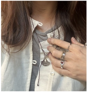 Dettaglio di anelli e collana vintage in argento S925 con gemma rossa su lino beige