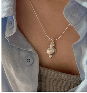 Detail of organic matte S925 silver pendant necklace worn on light blue linen shirt
