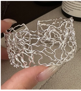 Detailed view of wide open silver bangle with organic flowing liquid metal mesh texture