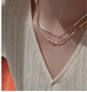Detail of gold and silver snake chains with baguette-cut zircon on a knitted V-neck top