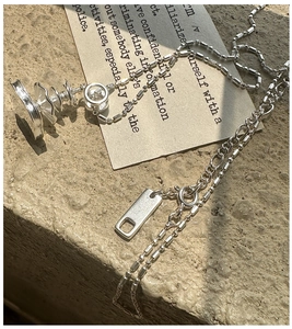 Detail of silver S925 necklace with spiral pendant and mixed chain on stone background