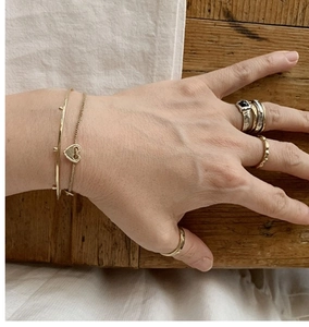 Detail showing layers of gold bracelets and zircon rings on a model hand with natural tones