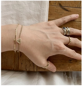 Close-up of layered silver and gold rings with zircon and heart bracelet on hand