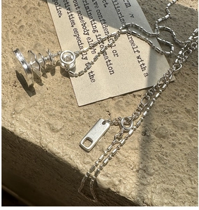 Artistic close-up of S925 silver layered chain necklace with irregular pendant on stone