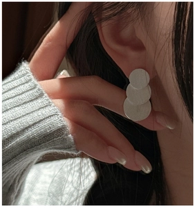 Detail of matte silver minimalist earrings featuring three stacked geometric discs on a model