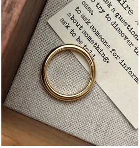 Close-up of a sleek gold-plated minimalist ring resting on a rustic wooden tray texture