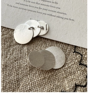 Macro detail of silver layered disc earrings with brushed finish on a rustic fabric background