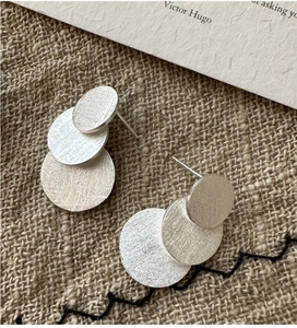 Macro detail of silver layered disc earrings with a brushed metal texture on linen background