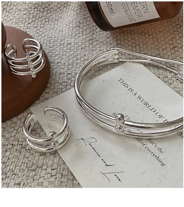 Detailed close-up of layered 925 sterling silver rings and cuff on a rustic wooden display