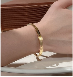 Gros plan d'un bracelet jonc doré minimaliste porté par un mannequin sur fond vintage