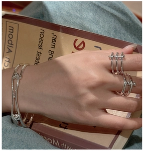 Close-up of S925 sterling silver double-layered rings and open cuff on denim and book