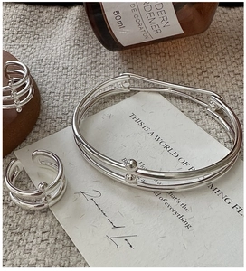Detail of minimalist S925 sterling silver layered bracelet set on textured fabric background