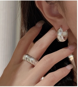 Detail of silver hoop earrings and ring featuring intricate CNC engraved woven texture