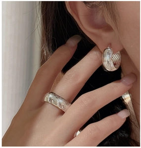 Detailed view of silver hoop earrings and wide ring with vertical textured stripes