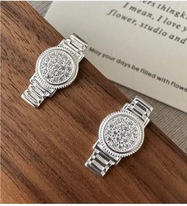 Vue macro de boucles d'oreilles en argent forme montre avec zircons sur socle en bois
