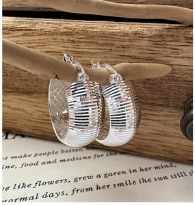 Détail de créoles en argent avec texture CNC horizontale sur une branche en bois