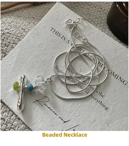 Detail of silver snake chain necklace with green beads on artistic textured card