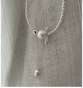 Detail of silver beaded necklace featuring polished metal bar and white teardrop pearl