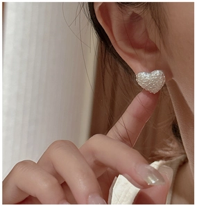Close-up of S925 silver heart earring with cream pearlescent texture worn by a model