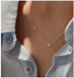 Close-up of minimalist S925 silver necklace with single round zircon on light blue linen
