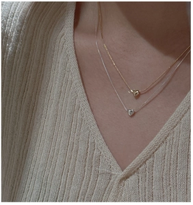 Détail de colliers cœur en argent S925 doré et argenté sur un pull en maille douce