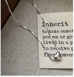Gros plan d'un collier pendentif cœur en argent S925 minimaliste sur fond de lin texturé