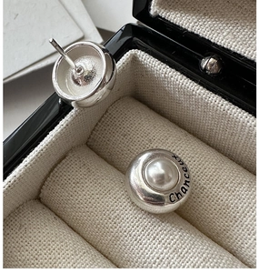 Macro shot of silver round earrings with white pearl and Chanceux engraving on band