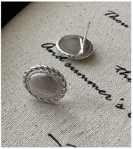 Detailed macro view of silver-tone oval stud earrings with brushed texture and twisted rope edge