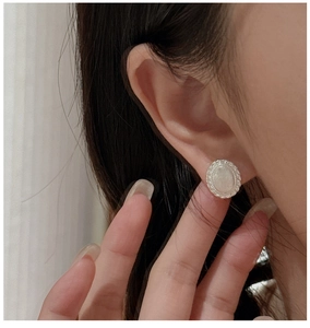 Close-up of S925 sterling silver earring with round embossed design and braided border