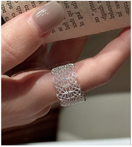 Detailed close-up of a wide silver lace pattern ring worn on the index finger