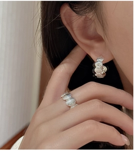 Detailed view of silver shell texture ring and matching earrings worn by a model