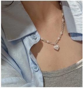Détail d'un collier avec pendentif cœur argenté et perles blanches sur un mannequin