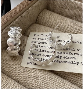 Macro shot of silver shell-shaped hoop earrings with wavy texture on jewelry box