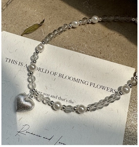 Détail du pendentif coeur en argent sur collier de perles blanches et perles facettées