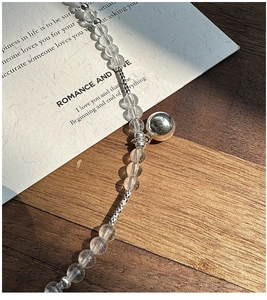 Macro detail of S925 silver beaded necklace featuring clear crystals and a round bell pendant