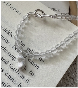 Dettaglio della fibbia a nodo in argento S925 e ciondolo a fagiolo su collana di cristallo