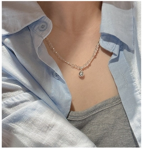 Detail of S925 silver beaded necklace with white crystals and round silver pendant on neck