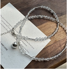 Detail of clear crystal beaded necklace featuring a silver bell pendant and lobster clasp